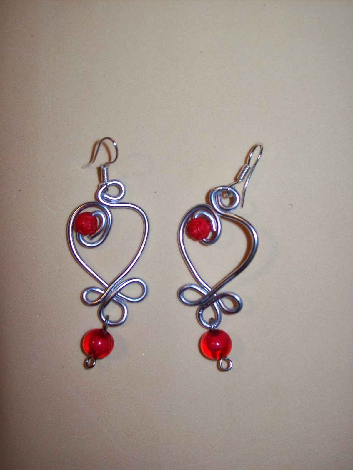Pendientes de alambre plateado con detalles de corazón y lazo y cuentas de vidrio rojo