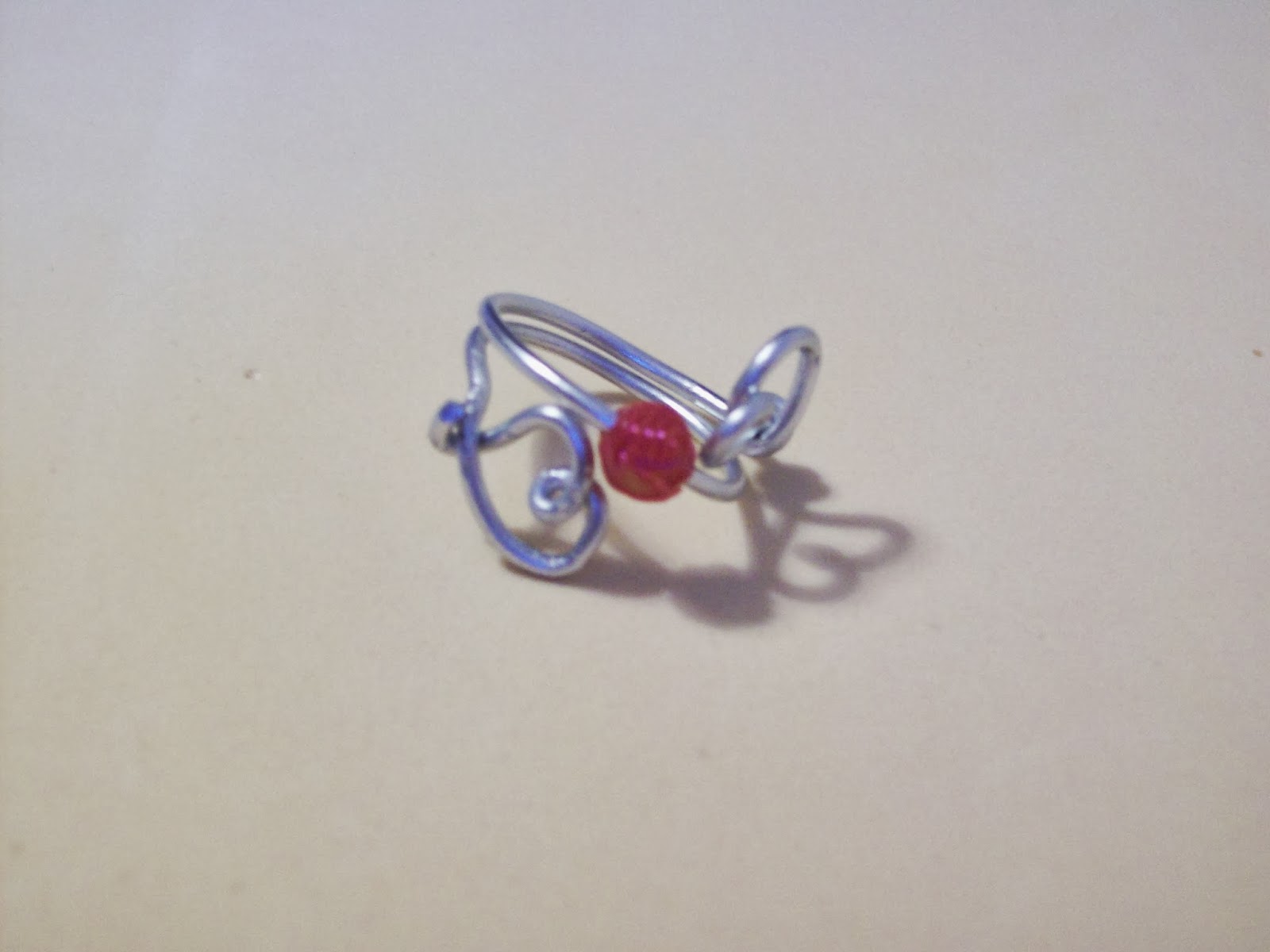 Primer plano de un anillo de alambre plateado con diseño en espiral y una pequeña cuenta roja